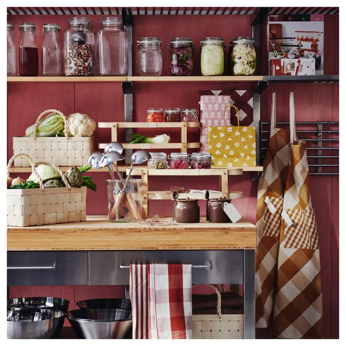 Kitchen counter with jars, vegetables, and kitchen utensils against a red wall.