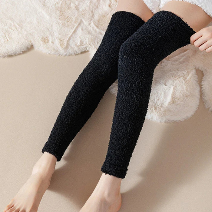 Seated person wearing black fuzzy thigh-high leg warmers on plush light surface - 