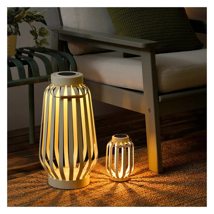 Two illuminated outdoor lanterns on a wooden floor with a couch in the background.