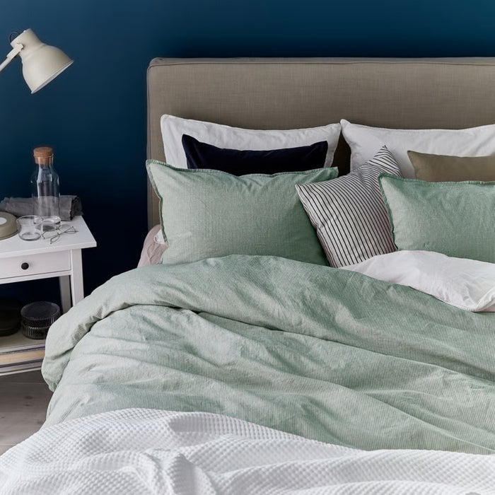 Bedroom with a bed featuring green bedding and pillows against a blue wall.