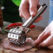 Person using a meat tenderizer on a piece of meat with a wooden cutting board in the background.
