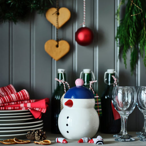 Snowman-themed candle with Christmas decorations on a table