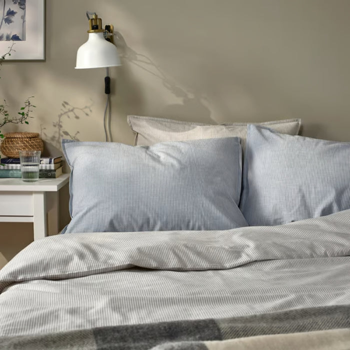 BERGPALM pillowcase, blue/striped, 50x80 cm. Shown on bed with matching duvet, white nightstand, books, and wall lamp – adds calm, lived-in charm to bedroom – 50577117.