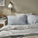 BERGPALM pillowcase, blue/striped, 50x80 cm. Shown on bed with matching duvet, white nightstand, books, and wall lamp – adds calm, lived-in charm to bedroom – 50577117.