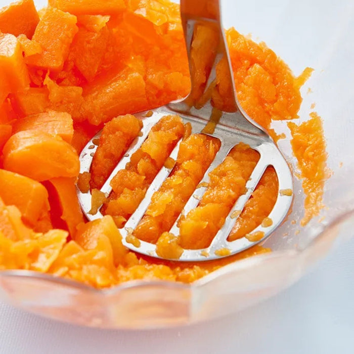 Stainless steel potato masher – close-up pressing orange vegetables in glass bowl for smooth consistency