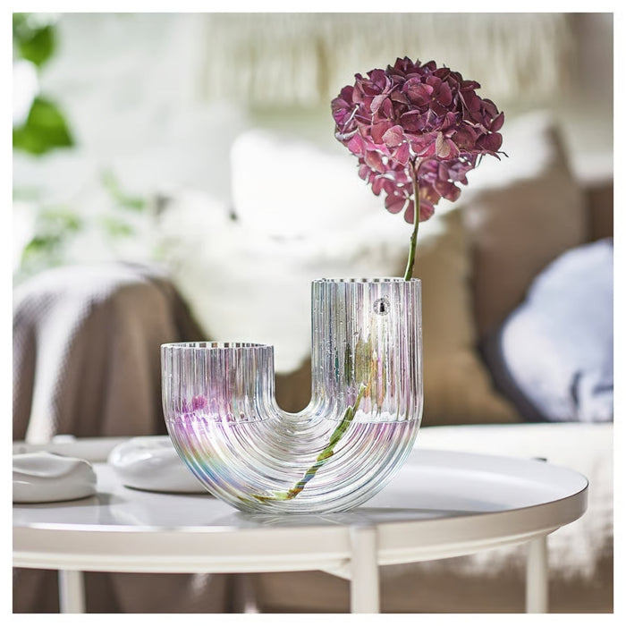 Decorative glass vase with pink flowers on a table in a blurred indoor setting