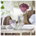 Decorative glass vase with pink flowers on a table in a blurred indoor setting