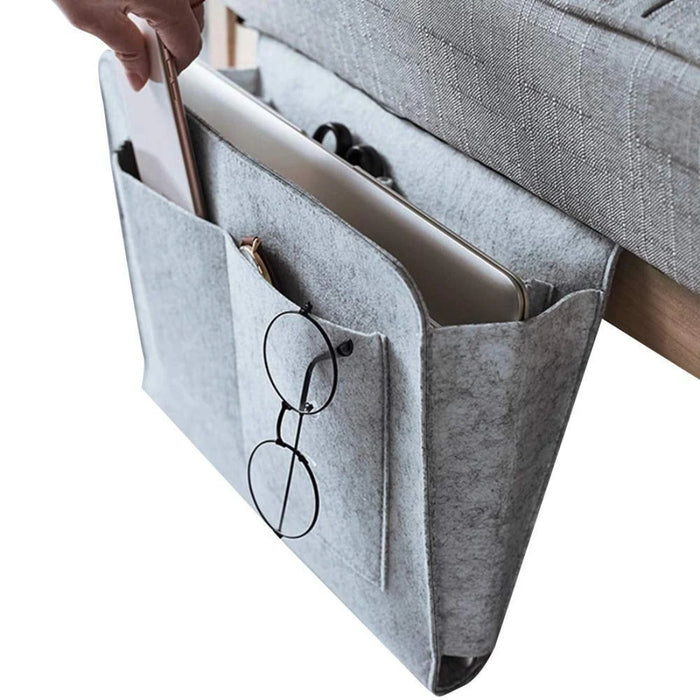 Gray fabric caddy with compartments holding a laptop, tablet, and glasses, attached to a piece of furniture.