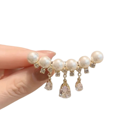 Pearl and crystal earring held by a hand on a white background