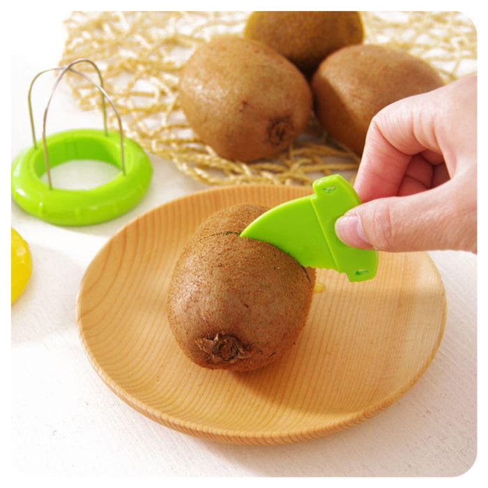 A hand uses a bright green fruit slicer to cut a kiwi on a light wood plate, with more kiwis and the green slicer visible in the background.