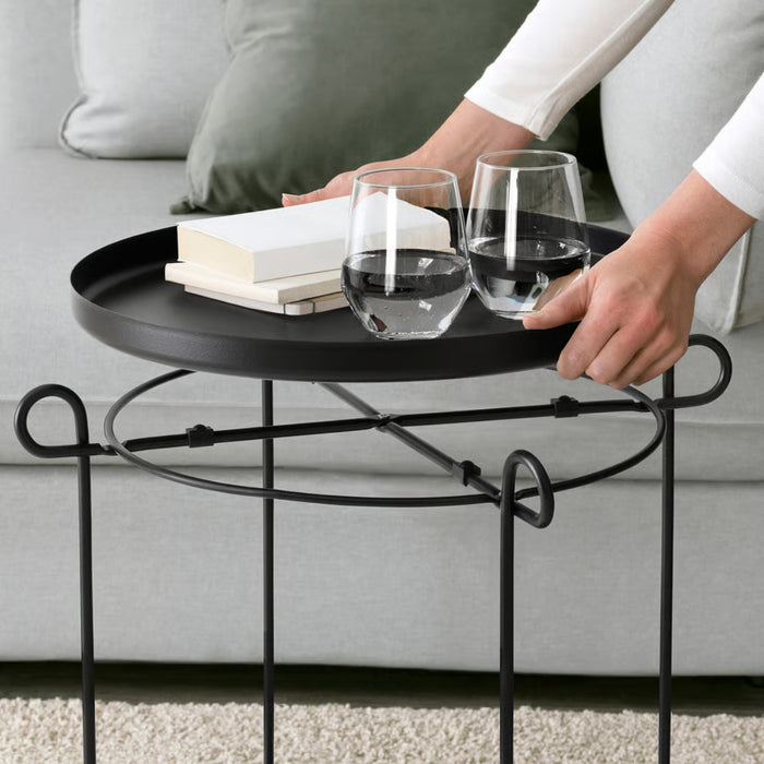 Black metal side table with books and glasses on a neutral background