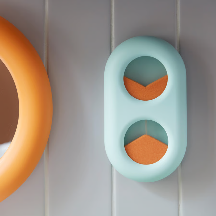 Light blue capsule-shaped wall organizer with two circular openings, each holding an orange foam wedge in opposite directions.