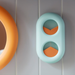 Light blue capsule-shaped wall organizer with two circular openings, each holding an orange foam wedge in opposite directions.
