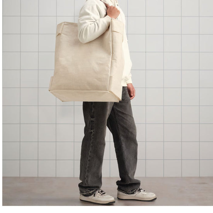 Person holding a beige tote bag against a tiled wall.