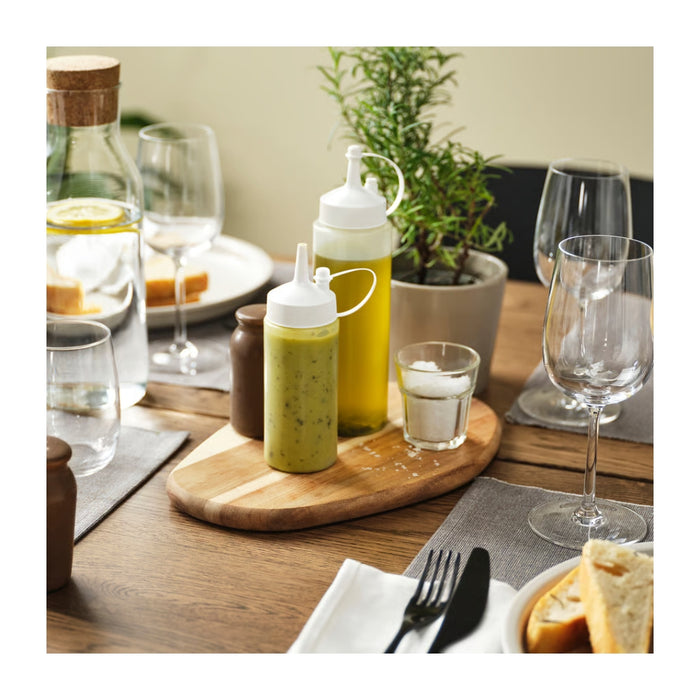 Dining table setup with condiment bottles, glasses, and a plant in the background.