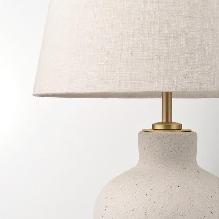 Detailed view of IKEA BLIDVÄDER lamp showing textured ceramic base, brass-toned fixture, and beige fabric lampshade with visible weave pattern.