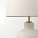 Detailed view of IKEA BLIDVÄDER lamp showing textured ceramic base, brass-toned fixture, and beige fabric lampshade with visible weave pattern.