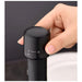 A close-up of a hand holding a black bottle stopper on a dark background.