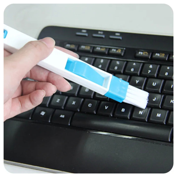 Hand holding a keyboard cleaning brush with blue bristles over a laptop keyboard.
