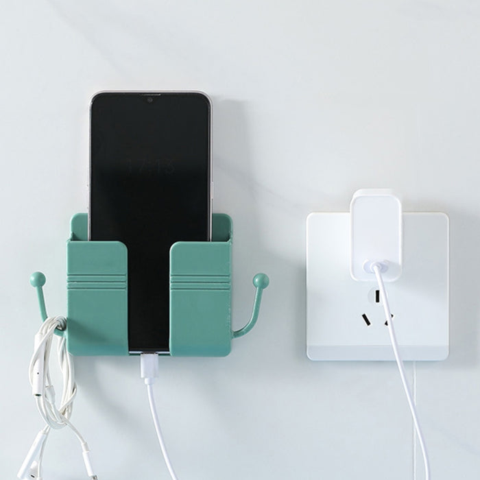 Green wall-mounted holder securing a smartphone and white charging cable; side hook holds white earphones—organized setup beside a wall socket, designed for multifunction charging and storage – 1598448185067 13069398.