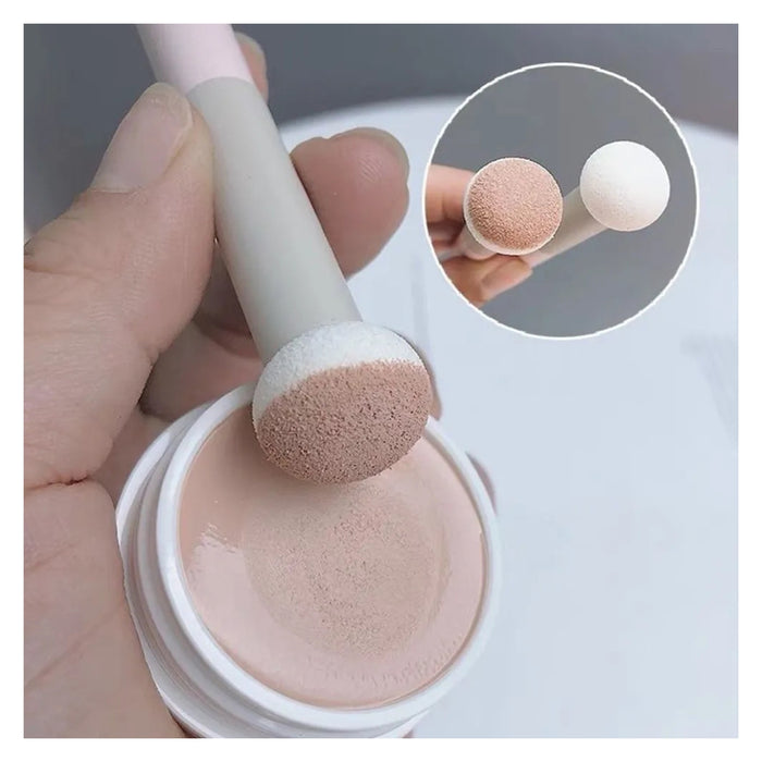 Makeup brush with pink bristle tip being used to apply cream from a container.