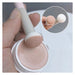 Makeup brush with pink bristle tip being used to apply cream from a container.
