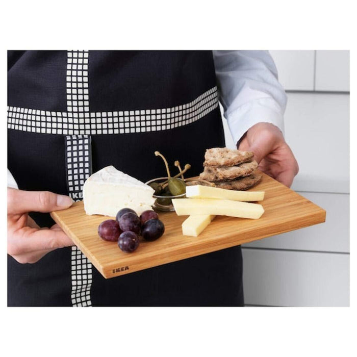 Person holding a wooden cheese board with cheese, grapes, and crackers.