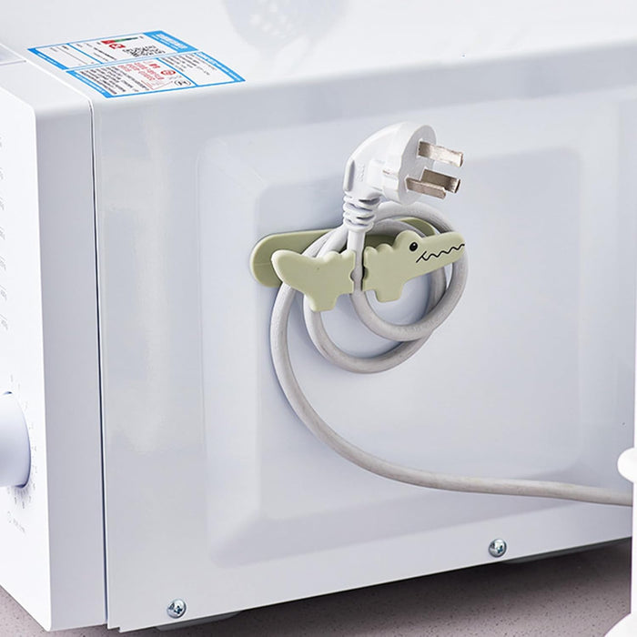 White electrical outlet with a coiled white cable and green dinosaur-shaped plug inserter.