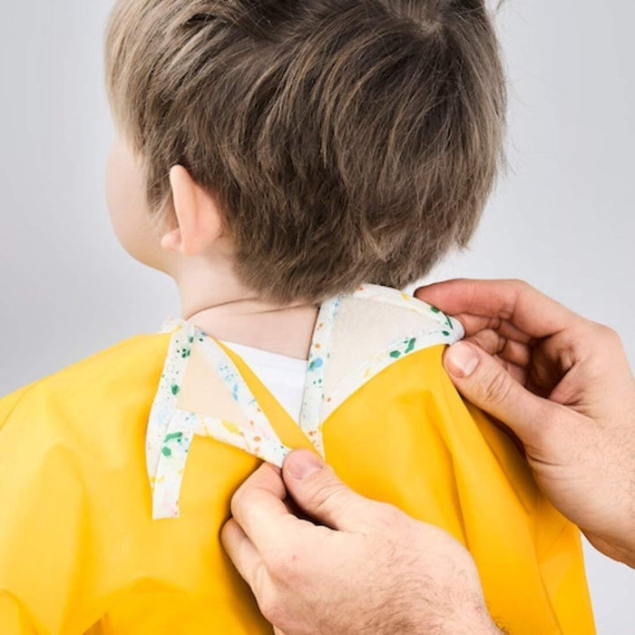 Person adjusting a floral collar on a child wearing a yellow outfit against a plain background