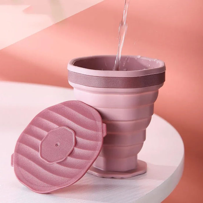Pink collapsible cup with a lid on a white surface against a pink background