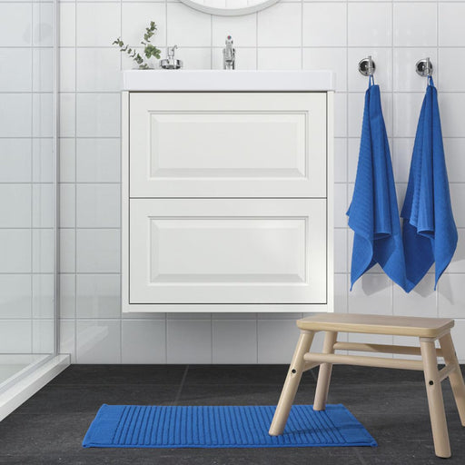 Bathroom with white vanity, blue towels, and a blue mat on the floor.