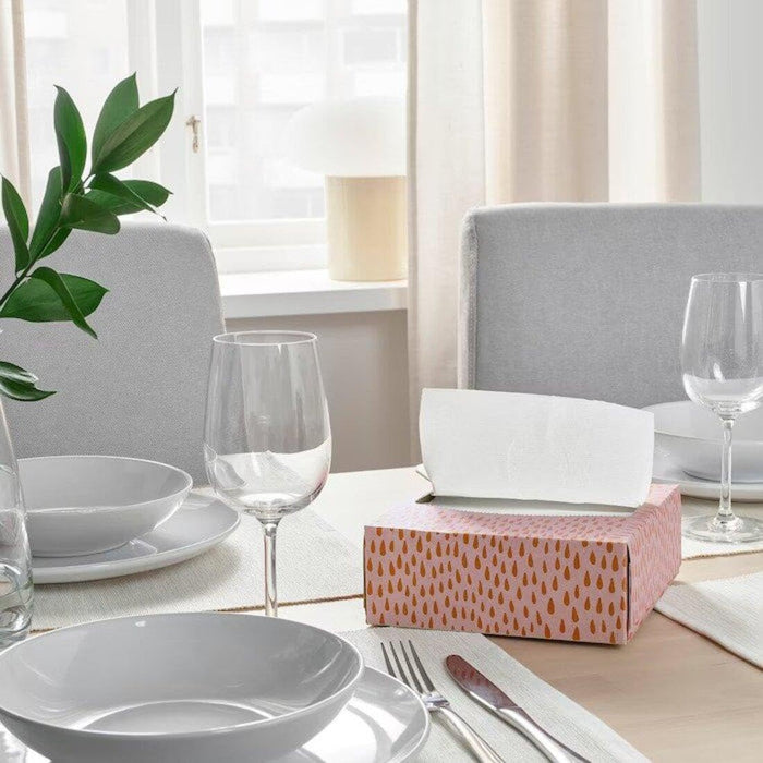 Dining table set with plates, glasses, and a pink box in a bright room.