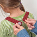 Person adjusting straps on a child's green and white striped shirt with red straps.