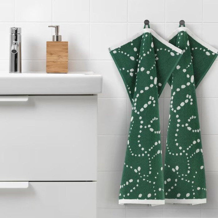 Green towels with white patterns hanging on a rack in a bathroom.