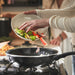 Person adding vegetables to a frying pan on a stove