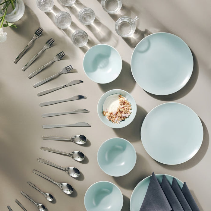 Light blue ceramic plates and bowls with silver cutlery on a beige surface