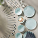 Light blue ceramic plates and bowls with silver cutlery on a beige surface