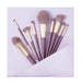 Set of makeup brushes with purple and gold handles on a light purple background