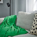 DAGGKÅPOR throw, green, 130x170 cm. Draped over light grey sofa with beige polka dot cushion and black floor lamp – adds cosy, vibrant touch to living space – 90602695.