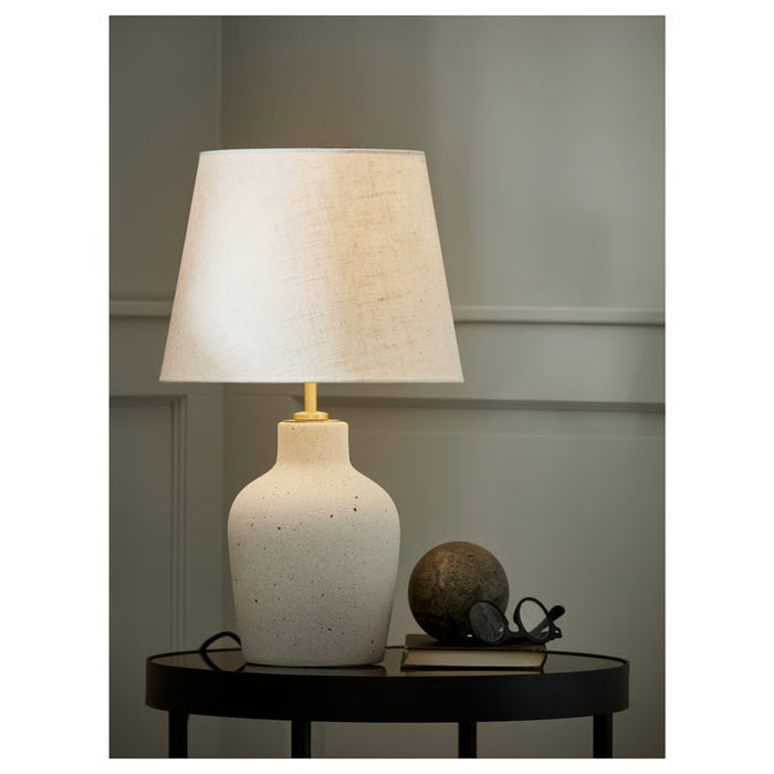 
Elegant ceramic table lamp with beige shade, styled on a black side table alongside books, eyeglasses, and a decorative sphere in a cozy living space.



