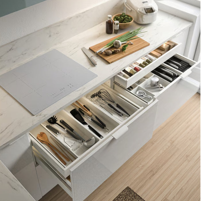 Open kitchen drawer with utensils and a cutting board on a marble countertop.