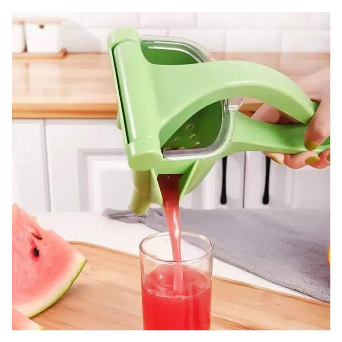 A hand using a light green manual citrus juicer to squeeze juice from a watermelon into a clear glass, set on a wooden cutting board in a kitchen.