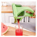 A hand using a light green manual citrus juicer to squeeze juice from a watermelon into a clear glass, set on a wooden cutting board in a kitchen.