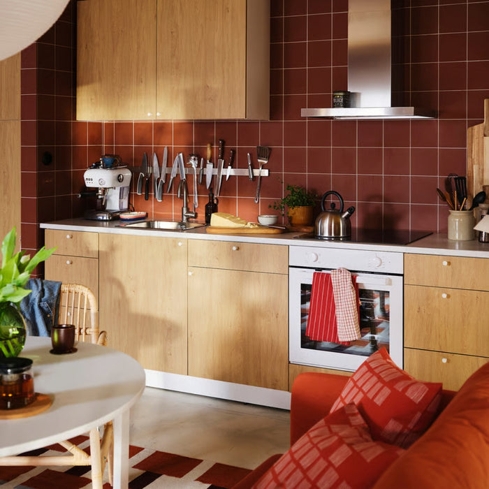 Modern kitchen with wooden cabinets, red tiled walls, and a sofa.