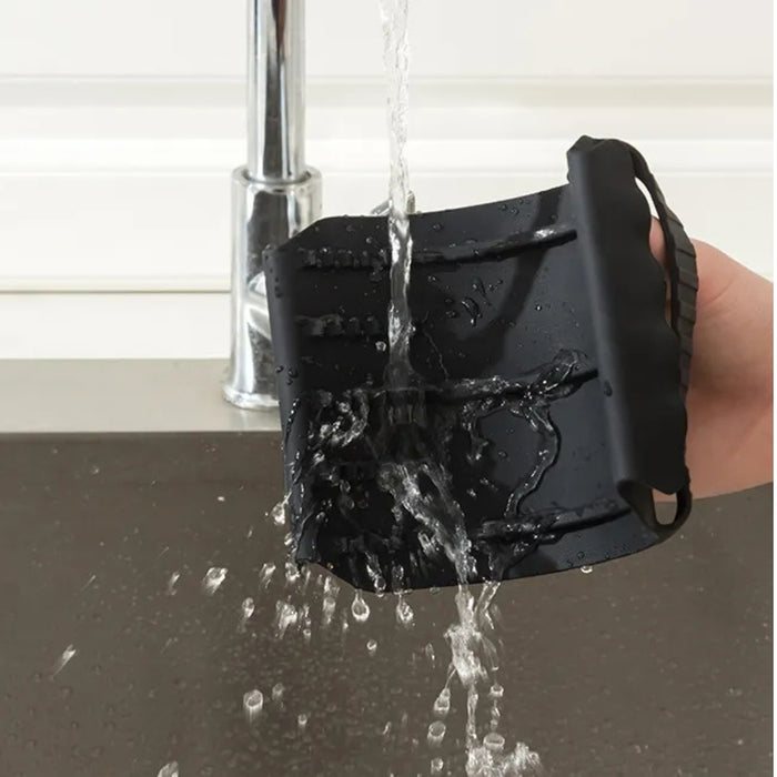Hand rinsing a black silicone dishwashing glove under a running faucet. The glove features textured scrubbing grooves on the palm and fingers, demonstrating its easy-to-clean, waterproof properties. Ideal for dishwashing and general kitchen cleaning tasks—combining protection with built-in scrubbing functionality.- 1598452898401 13017586