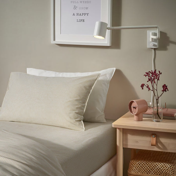 Neatly made bed with pillows and a nightstand with a lamp and small clock.