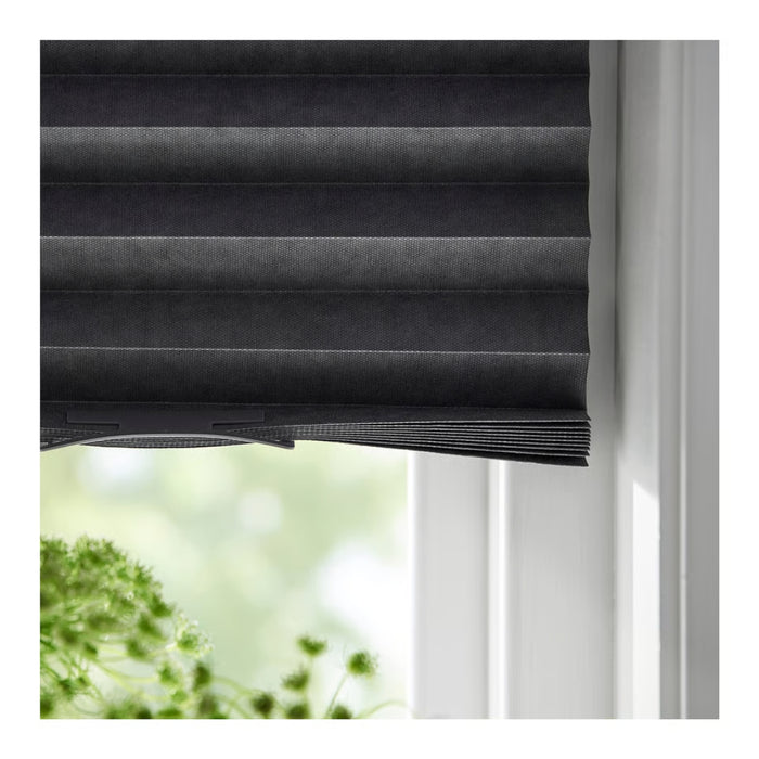 Black pleated blind with a blurred green outdoor background