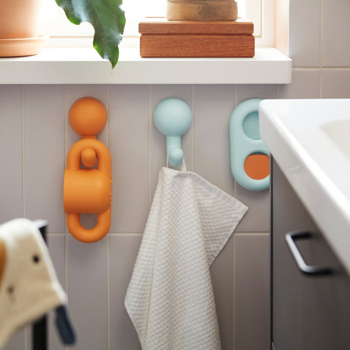 HUMLESJÖN hook mounted on tiled bathroom wall, holding a white towel beneath a windowsill with potted plant.

