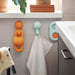 HUMLESJÖN hook mounted on tiled bathroom wall, holding a white towel beneath a windowsill with potted plant.

