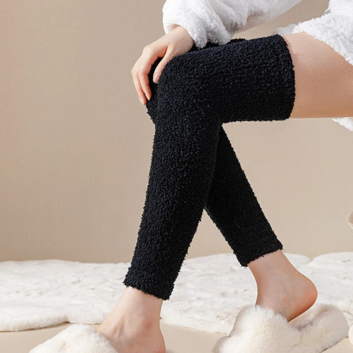 Person in white fuzzy outfit and black plush leg warmers with white slippers on soft surface - 